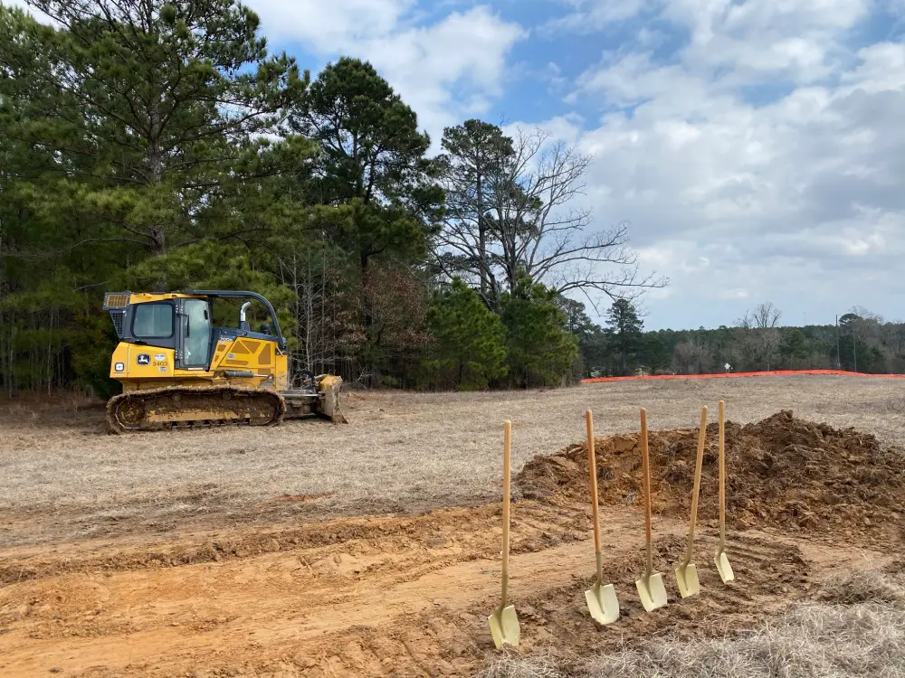 Construction site groundbreaking event with a dozer and golden shovels 